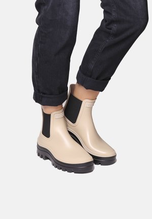 Beige rubber ankle boots with a black elastic panel, rounded toe, and rugged black outsole, featuring subtle branding on the upper.