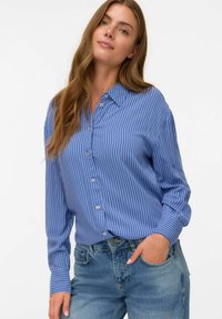 Blå knap-up skjorta med vita vertikala ränder, med krage, långa ärmar och en avslappnad passform, i kombination med ljusa denimjeans.