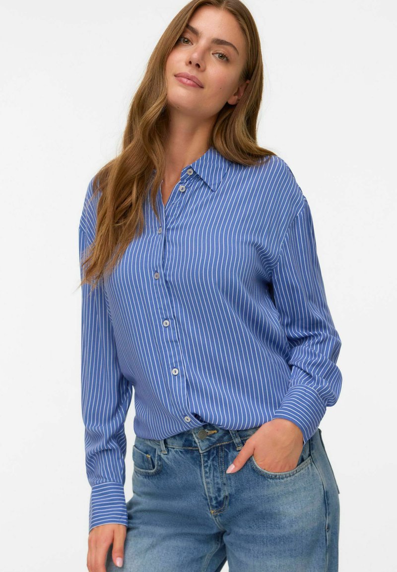 Blue button-up shirt with white vertical stripes, featuring a collar, long sleeves, and a relaxed fit, paired with light denim jeans.