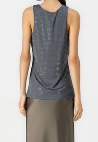 Top gris sin mangas con pequeños clavos metálicos distribuidos de manera uniforme, combinado con una falda oscura de oliva lisa, visto desde atrás.