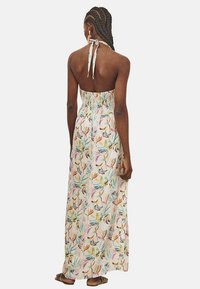 Vestido largo de tejido ligero, con un patrón floral multicolor, cuerpo elástico y lazo al cuello. La espalda está descubierta.
