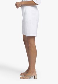 Witte linnen shorts met een op maat gemaakte pasvorm, zijzakken en een relaxte fit. Gepaard met zilveren sandalen met hakken en bandjes.