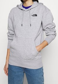 Šedá mikina s kapucí vyrobená z bavlněné směsi. Má přední klokaní kapsu a logo na hrudi. Hladké manžety a lem.