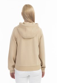 Felpa cappuccio beige con vestibilità rilassata, polsini e orlo a costine, texture morbida e un grande cappuccio, mostrata da dietro.