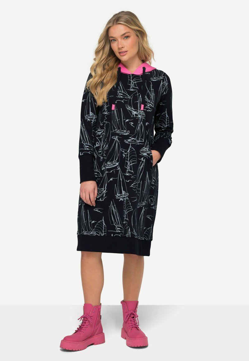 Schwarzes Hoodie-Kleid mit weißem Segelboot-Print, rosa Kapuze, Kordelzügen und langen Ärmeln; kombiniert mit klobigen rosa Stiefeln.