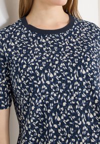 Femme portant un T-shirt bleu marine avec un imprimé léopard abstrait blanc et bleu clair et un col rond texturé.