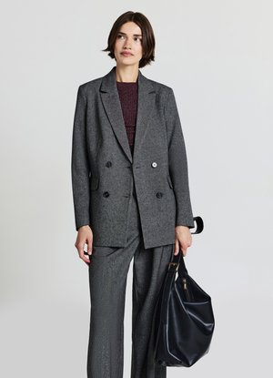Gray, double-breasted blazer with matching trousers, featuring a subtle texture. Model holds a black leather bag with a gold zipper accent.