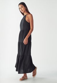 Mekkot pitkä musta maxi-tyylinen, jossa on kerroksellinen muotoilu. Ominaisuuksia ovat ohuet hihnat ja kevyt helma. Valmistettu kevyestä kankaasta, jossa on sileä rakenne.