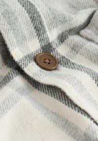 Gros plan d'un tissu à carreaux gris et blanc avec un bouton marron à quatre trous cousu au centre.