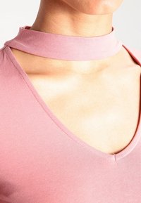 Staubrosa Bluse mit tiefem V-Ausschnitt und Choker-Kragen. Hergestellt aus glattem Stoff mit einer weichen, figurbetonten Textur.