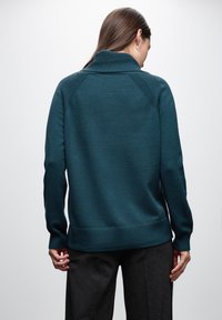 Teal stickad tröja med hög krage, texturerad axeldetalj, ribbade ärmslut och nederkant. Slätt tyg med en tight silhuett.