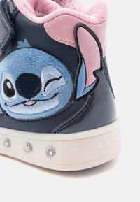 Zili un rozā sporta apavi ar pūkainā Stiča tēlu izšuvumu, Velcro siksniņu, teksturētu virsotni un baltu zoli, kas rotāta ar dekoratīvām dārgakmeņu imitācijām.