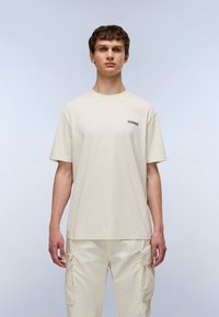 Lys beige bomulds t-shirt med korte ærmer, rund hals og et lille sort logo på brystet. Sammen med cremede cargo bukser.