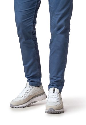 Witte en grijze sneakers met een gestructureerde suède afwerking, dikke rubberen zool en vetersluiting, gecombineerd met blauwe slim-fit broek.