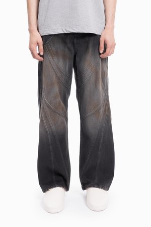 Pantalones de mezclilla anchos de color negro con una textura desvaída y patrones de costura diagonales, con un dobladillo deshilachado y un corte relajado.