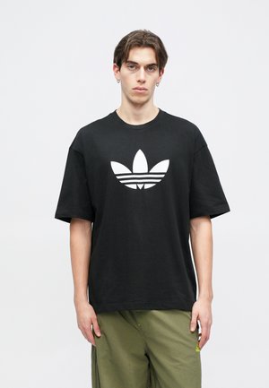 Svart bomulls-T-shirt med en stor vit Adidas-logotyp som består av tre bladliknande former och tre horisontella ränder under.