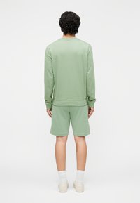 Sudadera verde claro y pantalones cortos a juego hechos de tela suave, con puños acanalados y un corte holgado. Se llevan con calcetines blancos hasta la mitad de la pantorrilla y zapatos beige.