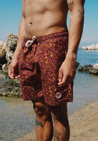 Bañador burdeos con un patrón abstracto colorido, cinturilla elástica y cordón blanco. Presenta un parche de logo en el dobladillo.