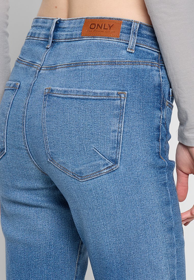Nahaufnahme einer Person, die hellblaue Jeans mit Gesäßtaschen und einem braunen Leder-Brand-Patch mit der Aufschrift "ONLY" trägt.