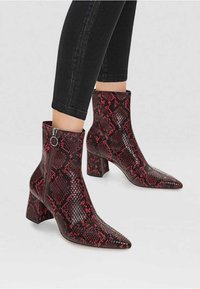 Bottines avec bout pointu et talon bloc. Présentent un motif en cuir de serpent rouge et noir ainsi qu'une fermeture éclair latérale avec un anneau de tirage circulaire.