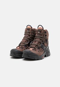 Brown hiking boots with black soles, textured upper, and round laces. Features a rubber toe cap, pull tab, and adjustable lace system.