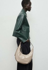 Chaqueta corta de cuero verde, jeans oscuros, sosteniendo un bolso hobo de cuero suave color crema con una sola correa.