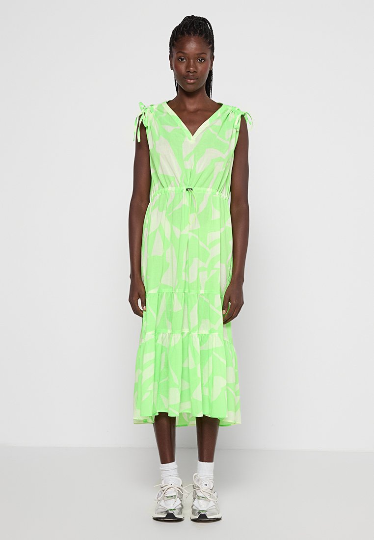 Zielona sukienka w wzory z głębokim dekoltem w kształcie litery V, z wiązaniem na ramionach i warstwowym fasonem spódnicy, wykonana z lekkiego, zwiewnego materiału.