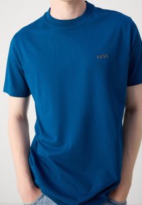 Modrá bavlněná tričko s kulatým výstřihem, krátkými rukávy a malým stříbrným logem "BOSS" na hrudi. Hladká textura a volný střih.