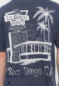 Tamsiai mėlynas marškinėlių audinys su balta grafine kepsninės ženklo ir tropinio peizažo su palmėmis, užrašu „San Diego, CA.“