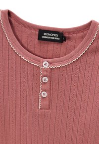 Haut à manches longues rose côtelé avec un col rond, trois boutons et des bordures délicates en dentelle blanche. Présente de petits motifs en œillets.