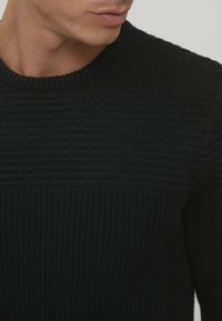 Schwarzer Strickpullover mit strukturiertem Design und horizontalen Rippungen an der Oberseite. Rundhalsausschnitt, mittlere Dicke und keine sichtbaren Verzierungen.