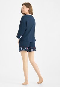 Granatowe piżamy składające się z długiego rękawa z mankietami w gwiazdki oraz dopasowanych szortów z motywami niebieskimi i kontrastującymi wykończeniami.