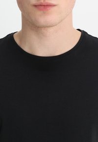 Camiseta de algodón negra con cuello redondo y textura suave. Sin patrones o logotipos visibles; diseño simple y clásico.