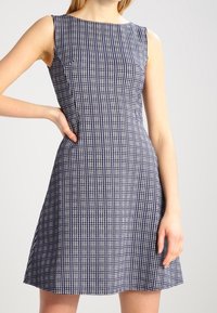 Robe sans manches à carreaux bleu marine et blanc avec un col rond, un buste ajusté et une jupe évasée. Tissu lisse avec des détails de texture subtils.