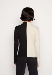 Gestreifter Langarm-Pullover in Schwarz und Creme, mit hohem Kragen und figurbetonter Silhouette. Glatte Textur, minimaler Hardware.