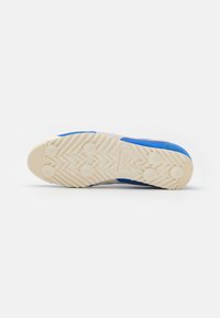 Semelle de basket blanche avec une surface texturée, présentant des accents bleus et des motifs de traction circulaires. Talon renforcé pour plus de durabilité.
