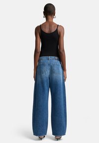 Svart ribbad linne topp i kombination med vida högmidjade blå denimjeans. Anmärkningsvärda detaljer inkluderar stora bakfickor och en urtvättad textur.