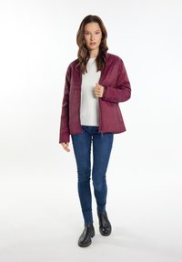 Bordeaux farvet pufferjakke med quiltet paneldesign, lynlås lukning og sidelommer, båret over en lysegrå sweater og blå jeans. Sorte ankelstøvler.