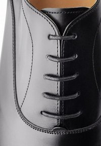 Zwarte leren dresschoenen met een gladde afwerking, een vetersysteem met zes oogjes en gedetailleerde stiksels langs de randen.