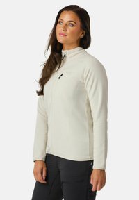 Light cream fleece jacket with a high collar, front zipper, and chest pocket. Smooth texture and fitted design, paired with black pants.