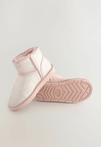 Un paio di pantofole rosa pelose alla caviglia con suole in gomma, una mostra l'interno morbido, l'altra mostra il motivo della suola e l'etichetta di taglia.
