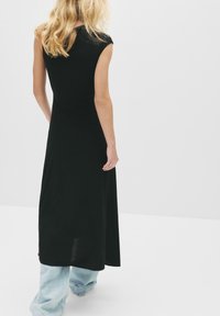 Sort ærmeløs maxi kjole med en tætsiddende overdel og en flydende skørt; modellen har lyseblå, løstsiddende jeans på under.