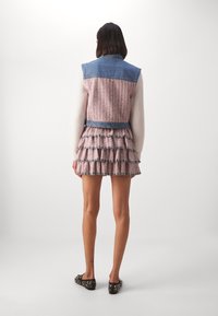 Veste en denim avec un corps en tweed rose, dotée d'un ourlet à volants et de bords effilochés. Portée sur un pull à manches longues avec un motif texturé.