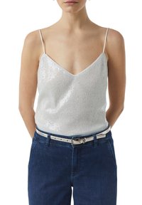Silver sequin top with a V-neckline and thin straps, paired with dark blue denim pants and a light silver belt. Textured, shiny surface.