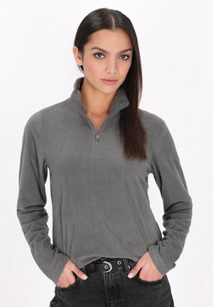 Grijze fleece pullover met een halve rits, lange mouwen en een zachte textuur, gedragen over zwarte high-waisted broeken.
