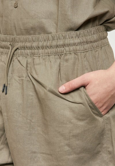 Pantaloni shorts in lino beige con vita elastica, dettaglio con cordoncino e tasche laterali. Il tessuto ha una texture liscia e una leggera lucentezza.
