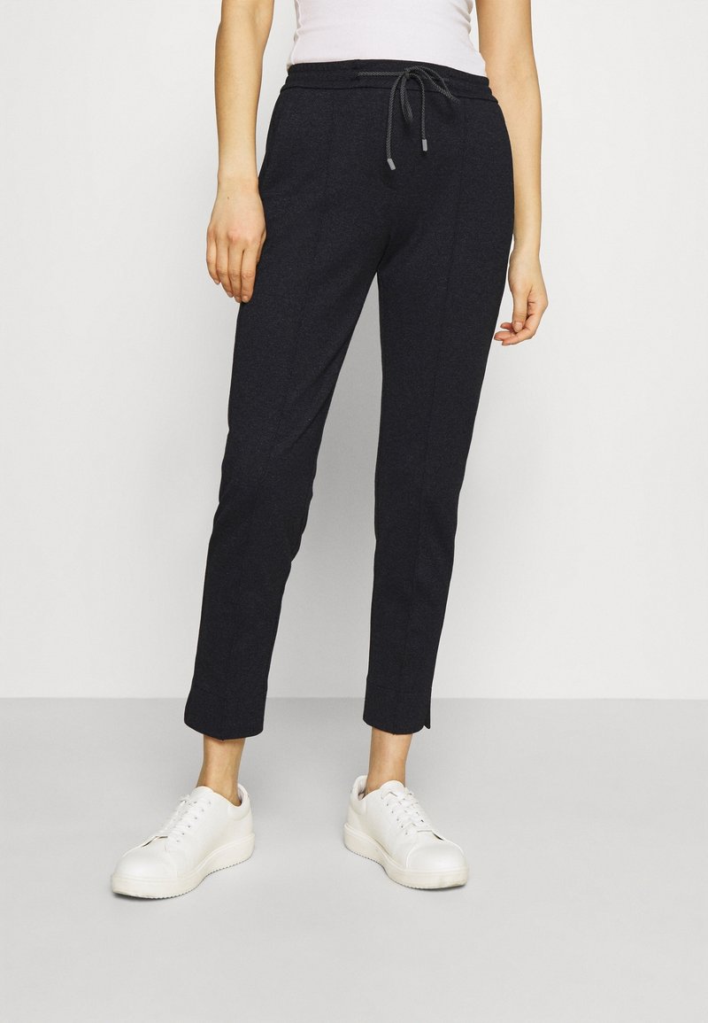 Dark navy jogger pants made from soft fabric, featuring a drawstring waistband, tapered legs, and two side pockets. Paired with white sneakers.