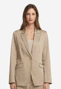Beige blazer med en enda knapp, sneddade slag och två framfickor. Tillverkad av ett slätt tyg, har en skräddarsydd passform och rak skärning.
