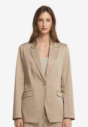 Blazer beige avec un bouton unique, revers crantés et deux poches devant. Fabriqué dans un tissu lisse, il présente une coupe ajustée et droite.