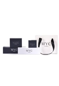 Cinque scatole con il testo "MYC PARIS": due bianche e tre nere, di dimensioni diverse, con una finitura opaca. Una borsa da shopping bianca abbinata con manici neri.